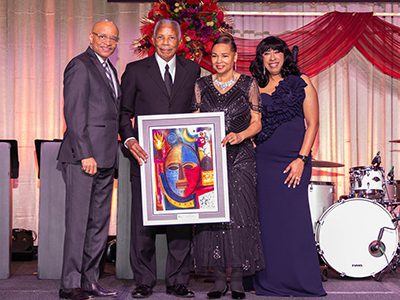 Four people holding a paining on stage
