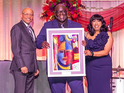 Three people holding a painting onstage