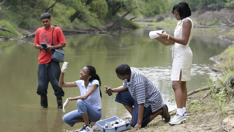Students standing by river analyzing water