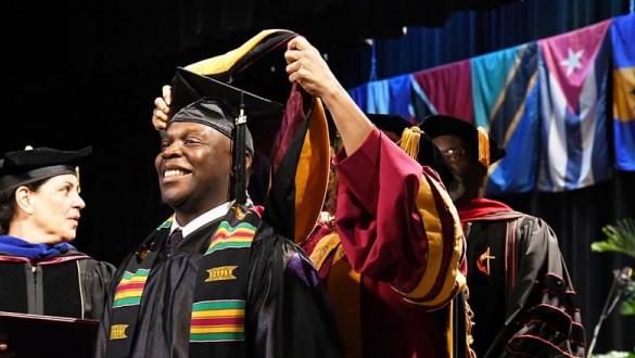 Male student at Bethune Cookman University receiving conferral during graduation ceremony wearing cap and gown