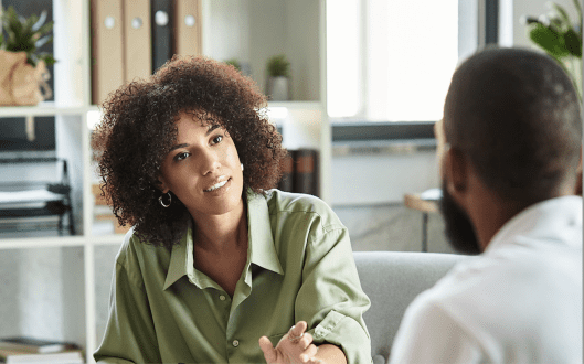 Black woman speaking with Black man in an office setting.