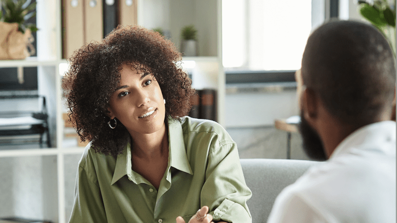 Black woman speaking with Black man in an office setting.
