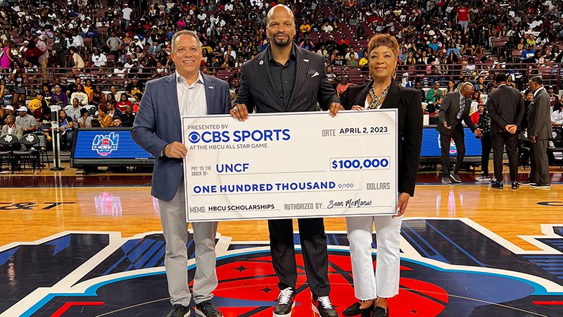Three people holding a novelty sized check on a basketball court