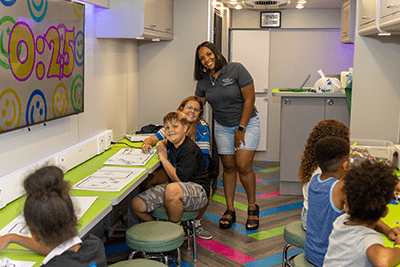 Group of kids enjoying Walk arts and crafts activities inside of a room. There is an adult posing with one of the children
