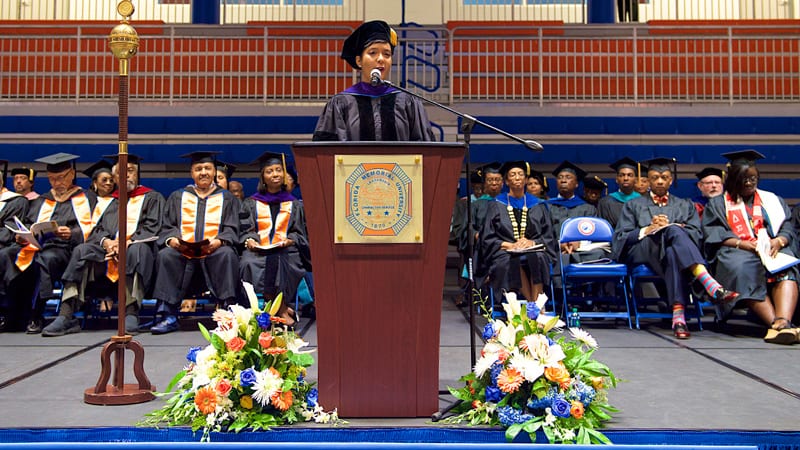Female student speaking at Florida Memorial University graduation ceremony wearing cap and gown