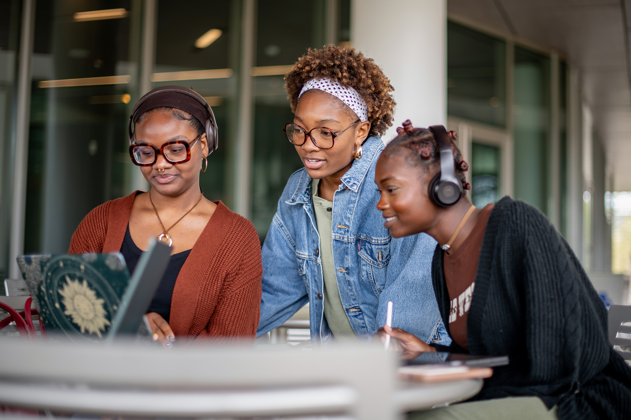 Three young women studying together, gathered around a laptop screen and discussing their work.