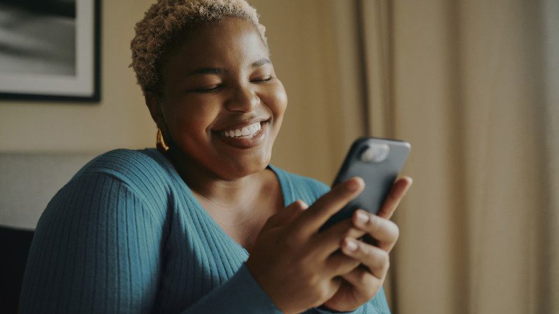 Smiling Young Black Woman Texting on Smartphone at Home