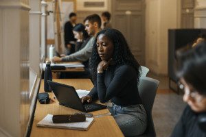 Black female student studying at her laptop, other students in the background and foreground are also studying.