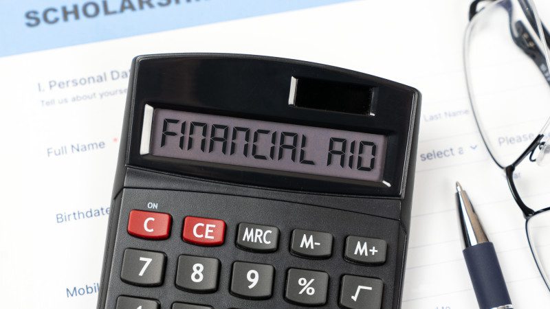 College scholarship application form with a calculator displaying the word Financial Aid on the screen, accompanied by eyeglasses and a pen