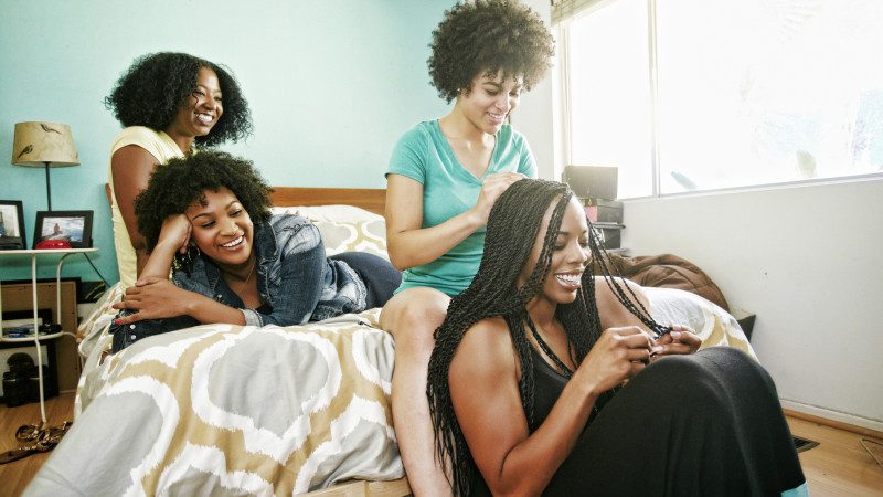 Woman braiding hair of friend in bedroom