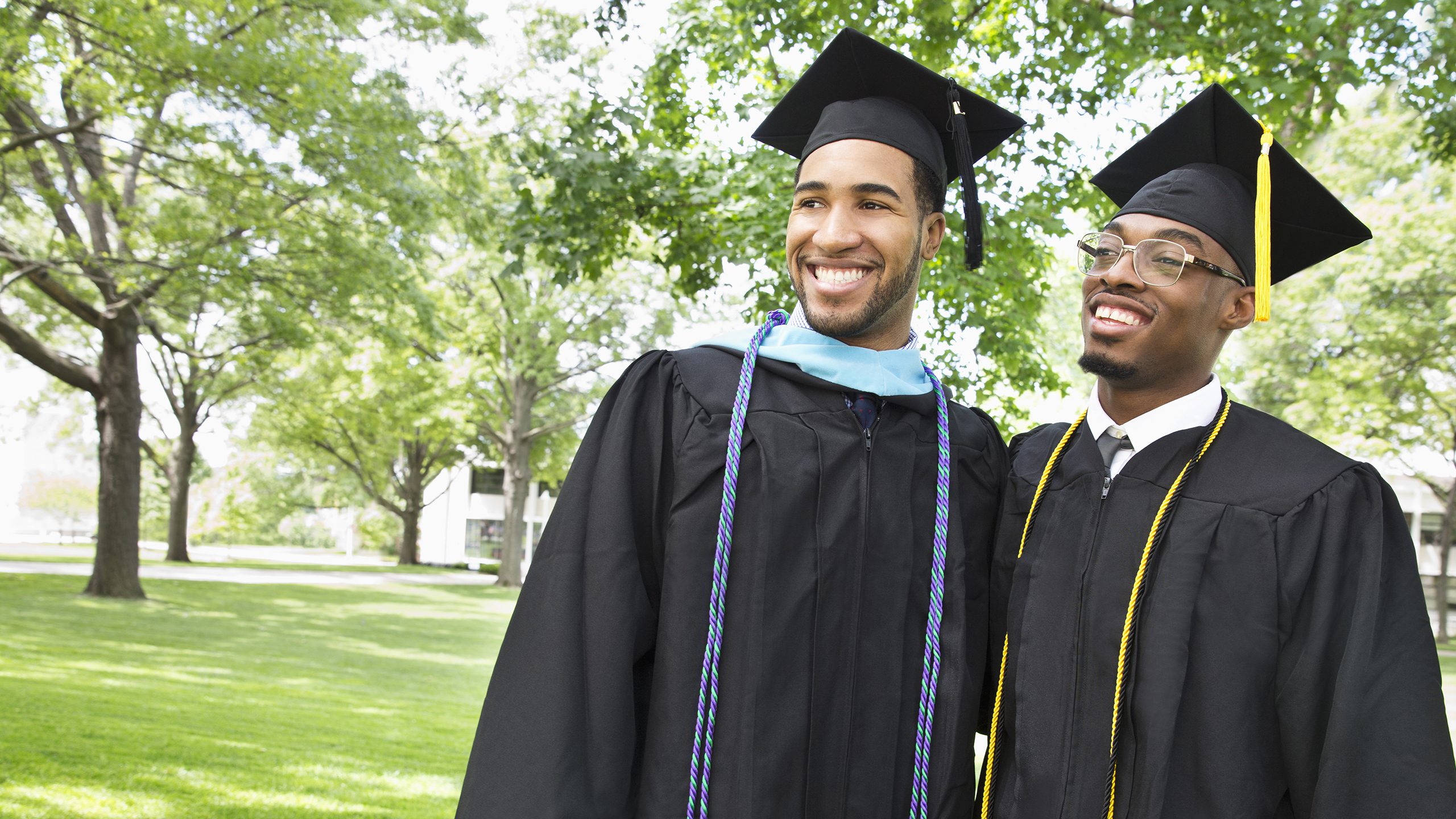 Hero Banner - two smiling male college graduates pose for pictures wearing caps and gowns