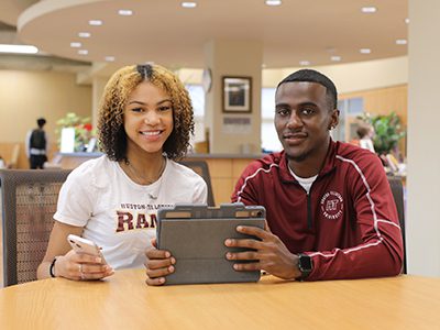 Two students sitting in a public space with a tablet
