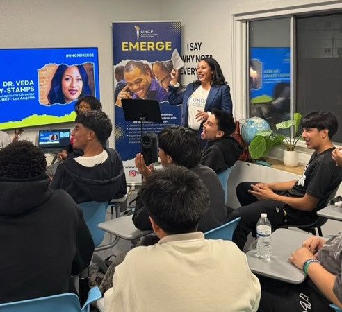 Dr. Veda Ramsay Stamps, regional development director, Los Angeles, UNCF, walks students and parents through applying for scholarships on UNCF's scholarship portal during an EMERGE College and Career Readiness Initiative workshop. Students sit in desks throughout the room.