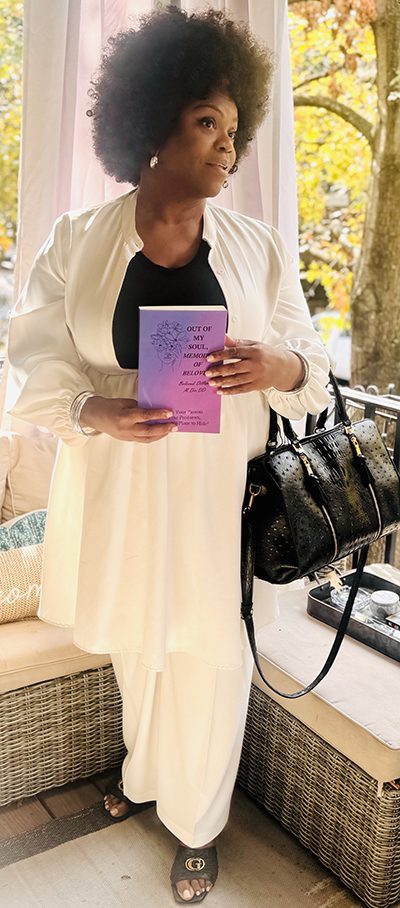 Beloved Dillard wrote Out Of My Soul: Memoirs of Beloved, a powerful testimony of her own experiences as a survivor of childhood sexual abuse, and has become a nationally recognized advocate for survivors of sexual and domestic abuse. She wears a white linen suit, black shirt, a black purse, and is holding up her book, which is a purple and pink gradient on the cover with a line drawing of a woman with flowers on her head.