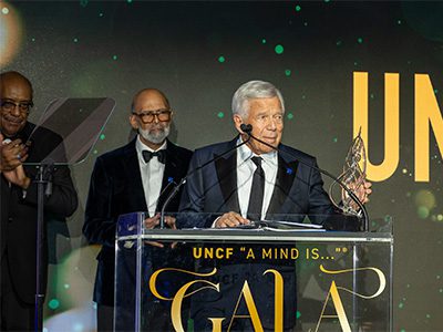 Man on stage. Two other men look on from behind