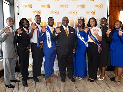 Large group of event attendees in front of step and repeat. All of the are holding up their hand it mimic a claw