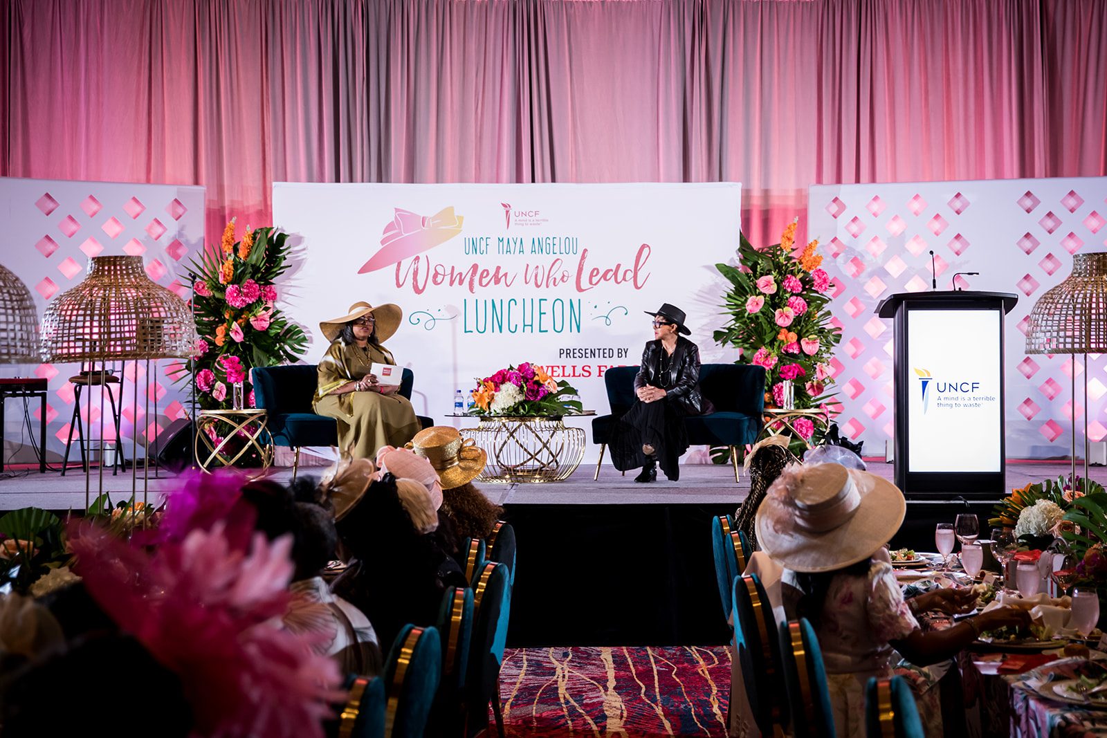 Two women seated on stage. Looks like they are having a discussion, part of the crowd is in view