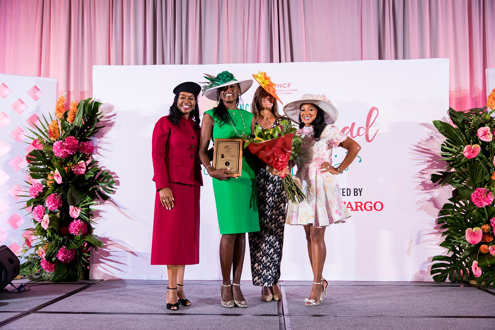 four female event attendees on stage, two in the middle are holding a plaque and flowers, respectively