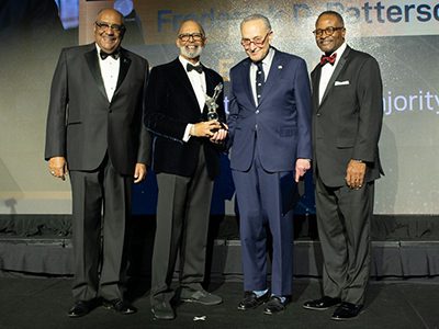 Dr. Lomax and Senator Charles Schumer with two other event leaders pose together onstage