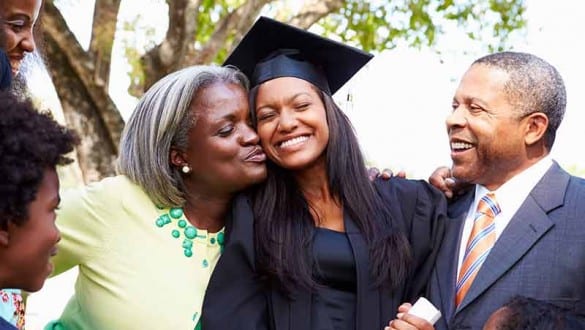 family celebrating with female college graduate in cap and gown with diploma