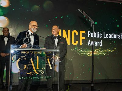 Dr. Lomax on stage with another gentleman. Another man looks on from behind