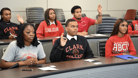 Students sit in a classroom and raise their hands at Clark Atlanta University.