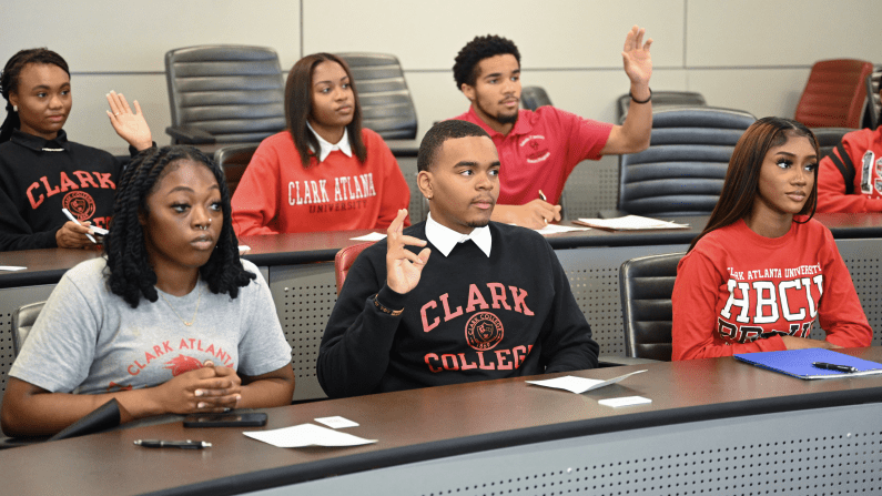 Students sit in a classroom and raise their hands at Clark Atlanta University.