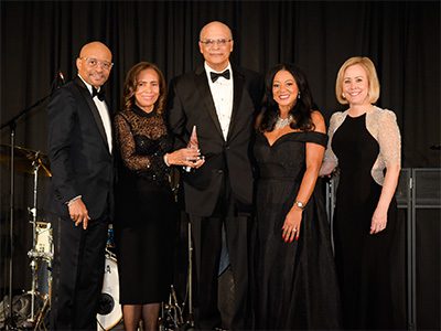 Group of five event attendees. The two in the middle are jointly holding an award