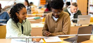 Two Black students discuss an assignment together in the library.