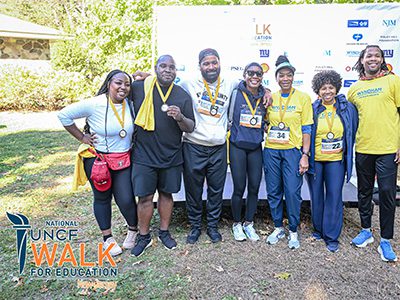 group of event attendees posing in front of step n repeat. They have medals around their necks
