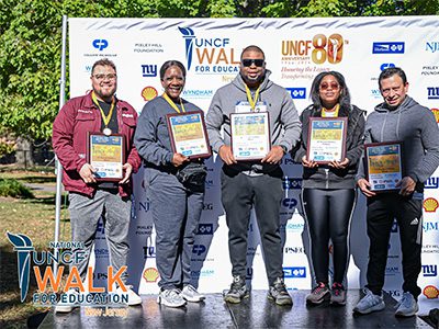 group of event attendees posing in front of step n repeat. They are holding plaques