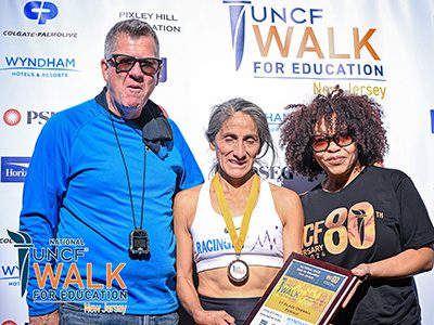 three group attendees posing in front of step n repeat. Person in the middle has a plaque