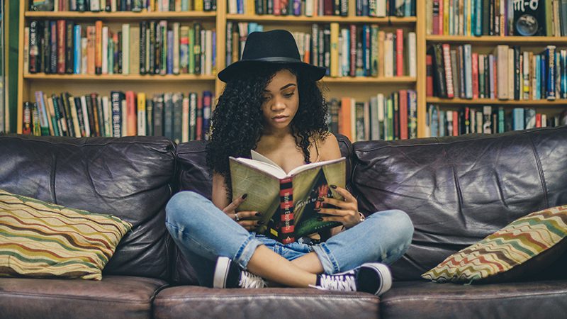 A girl sitting on a couch reading a book