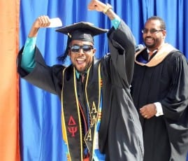 College graduate wearing hat and cloak cheering after formally graduating