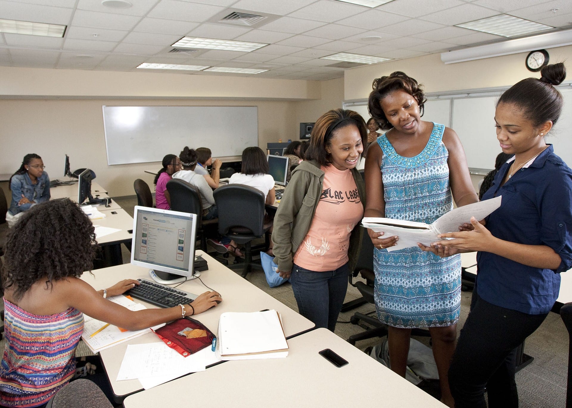 Image of a professor and several students working together in classroom near computers