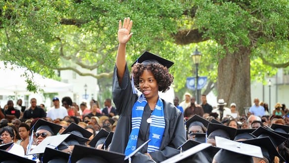 Female Dillard University student raising her hand during graduation ceremonies and wearing her cap and gown