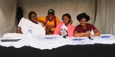 Group shot of 4 UNCF Walk Volunteers manning t-shirt table at event