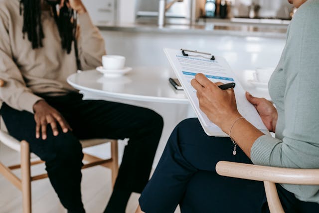 Hiring manager holding a resume in a clipboard across table from a Black job applicant