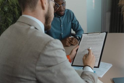 Black student in a job interview with a White hiring manager who is holding a resume on a clipboard