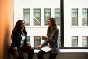 Two professional women in conversation in front of an office window