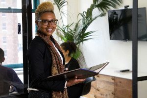 A Black woman standing in an office holding a binder. Photo by The Jopwell Collection on Unsplash.