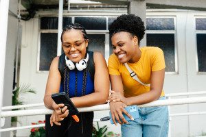 Two smiling women looking at a smartphone outdoors. Photo by Sandisk on Unsplash.