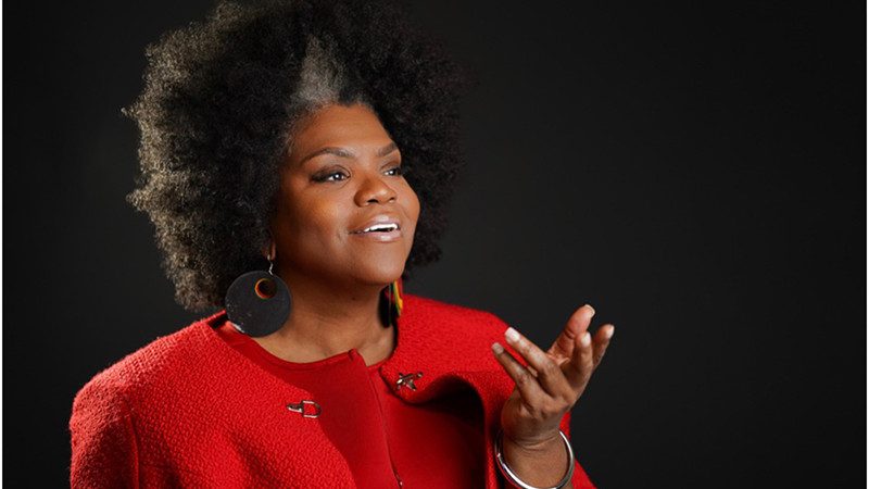 Beloved Dillard felt called to ministry ever since she was a young girl. She received a master’s of divinity at Interdenominational Theological Center in Atlanta, GA, and is in the second year of her doctoral of ministry degree. She is looking into the distance, holding out her hand, wearing large dangling earrings, and a red jacket.