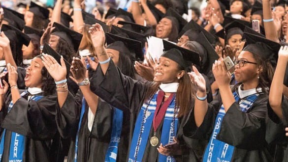 Group shot of Spelman College graduates cheering during graduation ceremony and wearing caps and gowns